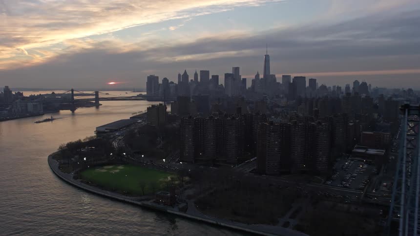 A breathtaking 5K aerial view of the Lower Manhattan skyline capturing both the Manhattan Bridge and Williamsburg Bridge from the Lower East Side public housing area during a winter sunset