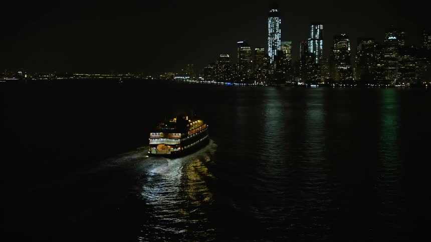 Aerial video clip of the Staten Island Ferry sailing through New York Harbor at night with a clear view of the Lower Manhattan skyline in winter