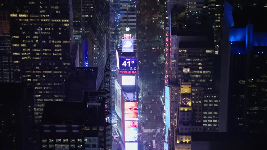 An aerial approach to the iconic Times Square New Years ball and large screens at night in winter in New York City