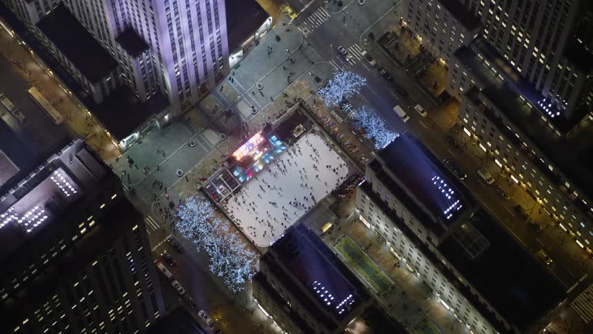 A night-time aerial view of the Rockefeller Center skyscraper is shown orbiting to reveal the ice skating rink below in Midtown Manhattan during winter