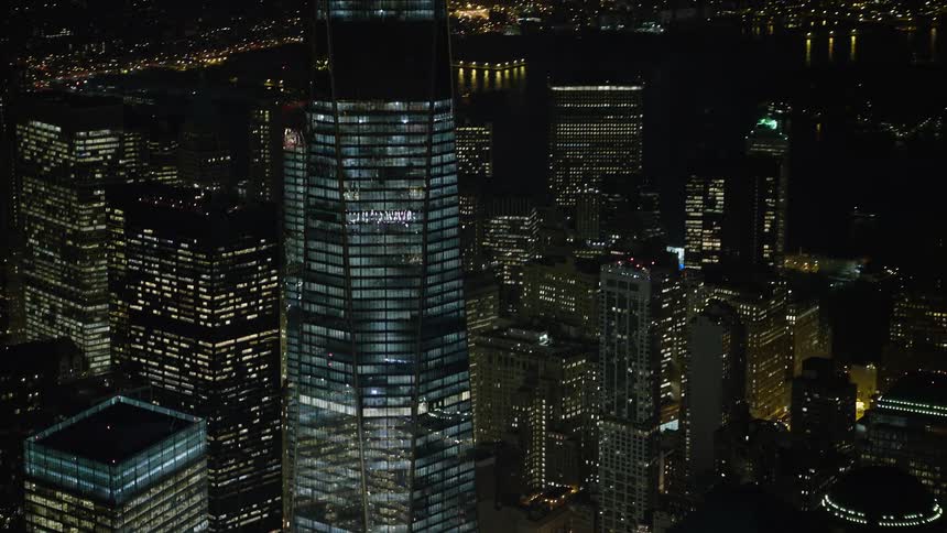 An aerial shot of the iconic One World Trade Center in Lower Manhattan is captured by orbiting and tilting up at night during a clear winter evening showcasing the modern high rise in the metropolis
