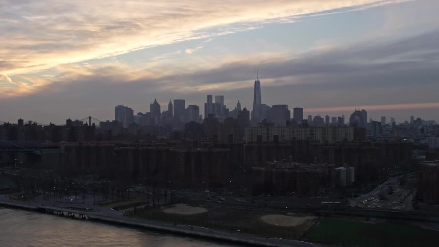 Aerial footage of Lower Manhattan skyline at sunset viewed from public housing by the East River on the Lower East Side with a cloudy winter sky and high-rise buildings towering over residential neighborhoods