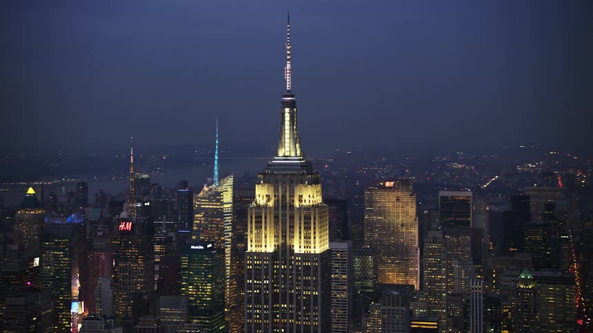 An aerial orbit of the iconic Empire State Building during winter twilight in Midtown Manhattan with other well-lit high rises in the background