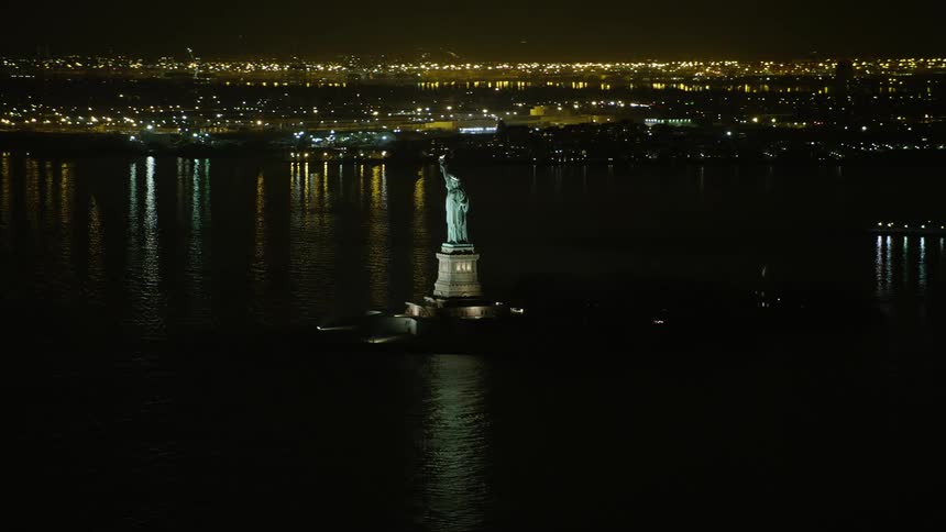 Statue of Liberty shining bright at night with Liberty Island and New York Harbor in the background