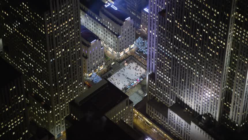 Orbit around Rockefeller Center at night to reveal the iconic ice skating rink in Midtown Manhattan during wintertime