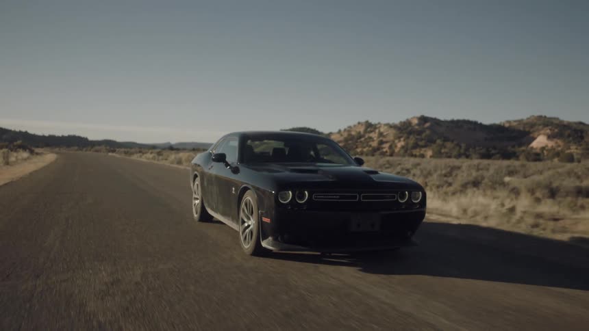 A black car drives down a road on a sunny day