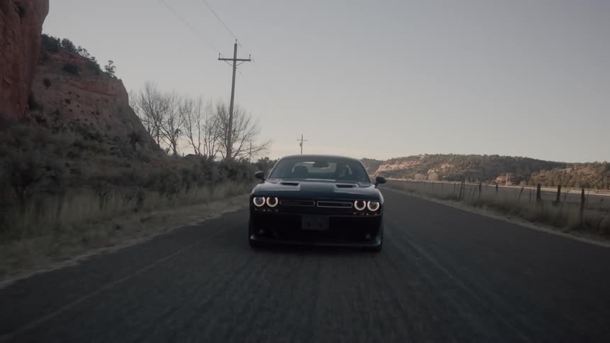 A black car traveling down a deserted road in the day