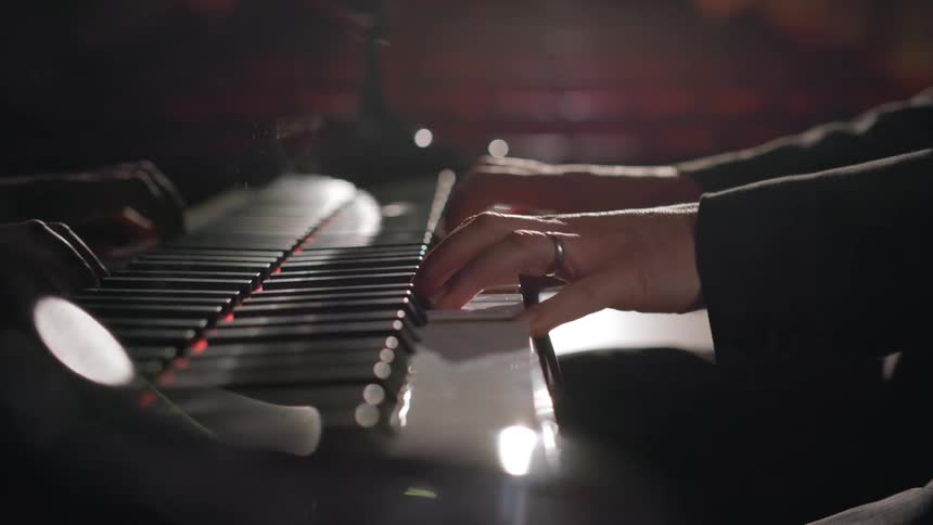 A man is sitting at a piano and playing music with both hands on the keys