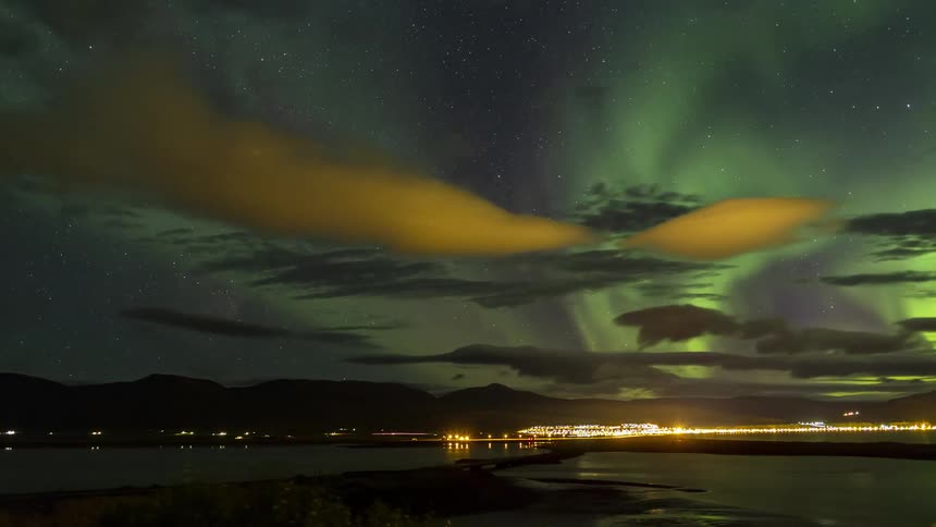 Traffic flows along road through water at night as northern lights shine in sky