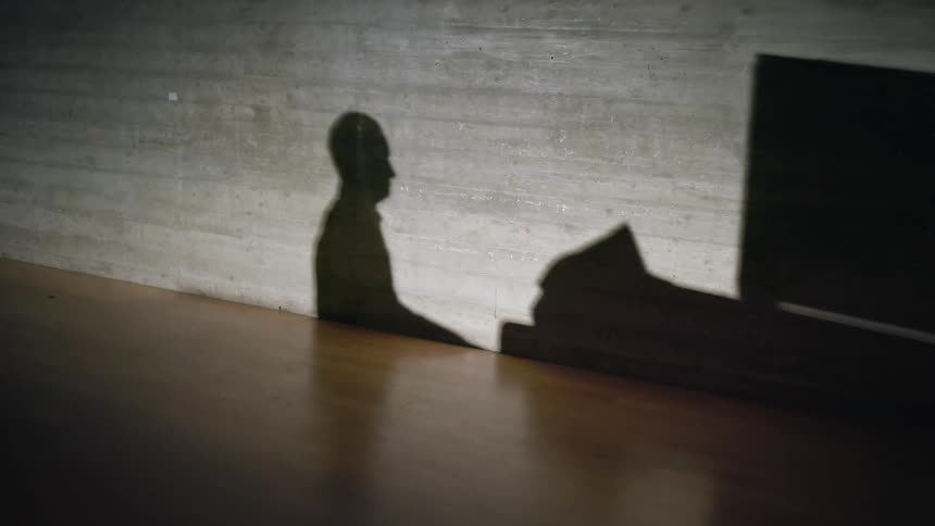Silhouette of a man playing a piano near a brick wall