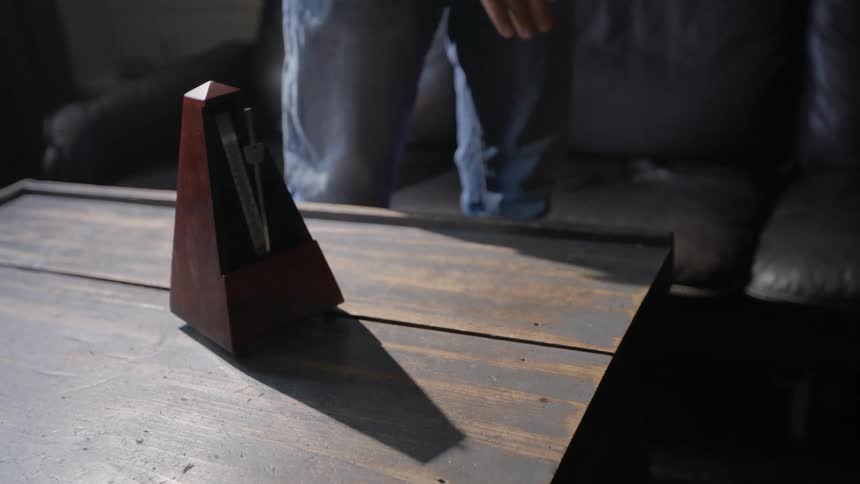 A person walks past a metronome and starts it with their finger