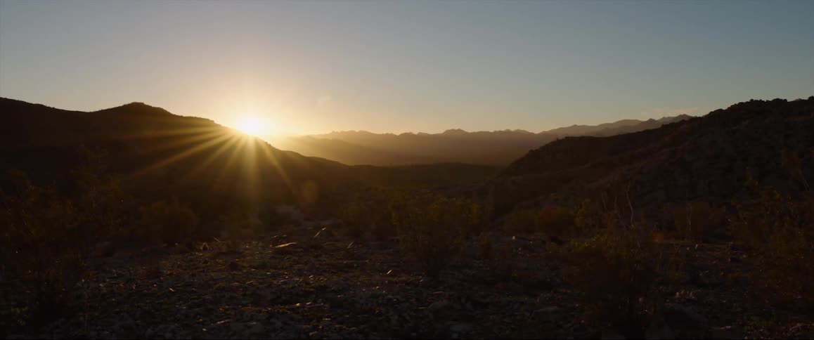 The sun shines brightly over mountaintops in a clear sky