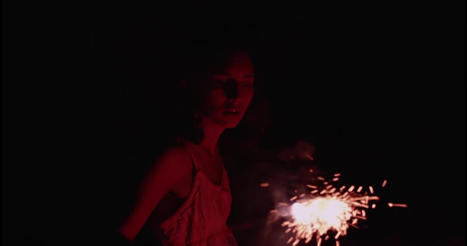 A woman is holding a lit firecracker and blowing on it