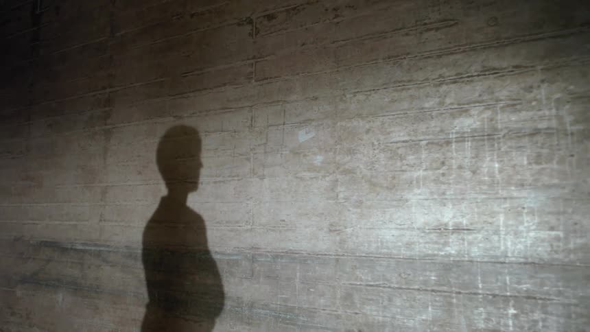 The shadow of a man is on a wall as he turns his body