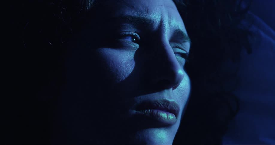 A flashing light shines on a womans face as she looks around in the darkness