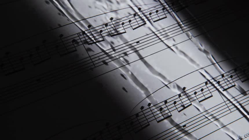 A page of sheet music can be seen in the darkness behind glass with drops of water rolling down it
