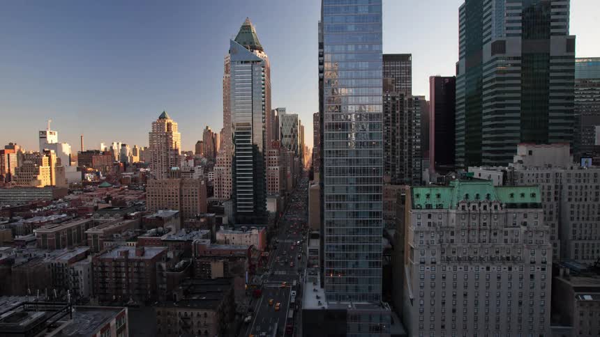 Aerial view of people walking down busy city street with and vehicles driving on highways between high rise buildings at dusk in new york city