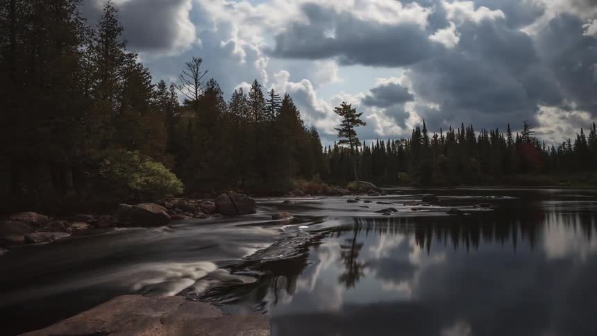 Clouds pass over a river through a forest during the day