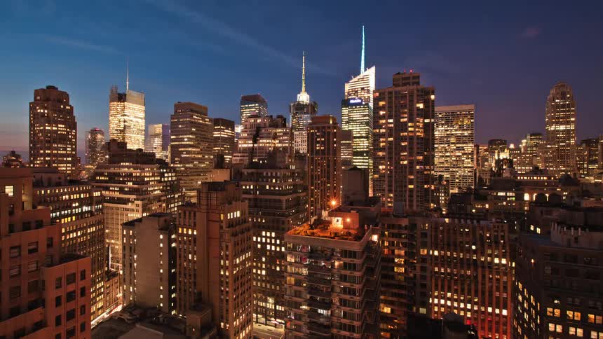 Lights illuminate the city buildings as darkness arrives