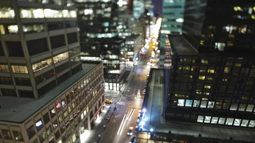 Vehicles travel down the city street at night with their headlights on