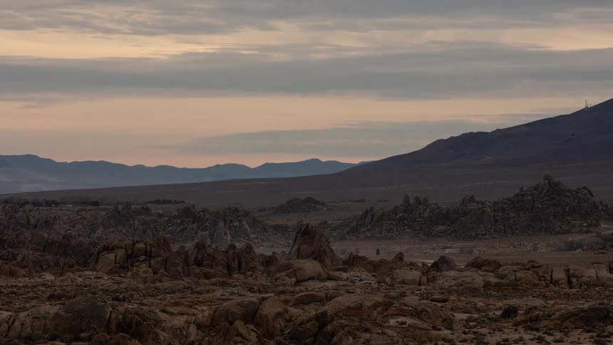 Rock formations stand in the desert badlands as clouds move over the mountains and darkness falls