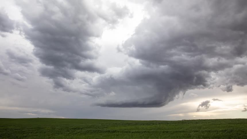 Storm clouds are moving in rotation over an open grass field