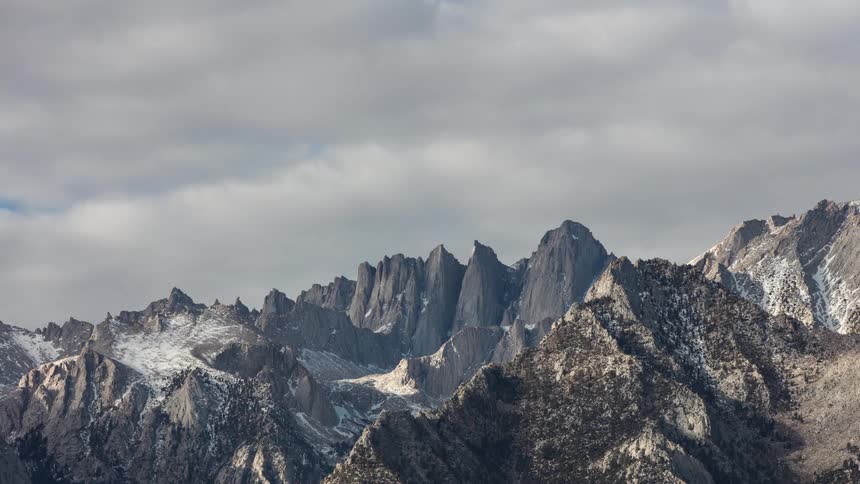 Clouds pass swiftly overhead above a jagged mountain range