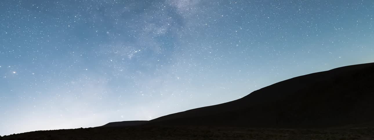 The stars of the milky way move across the night sky over the hills and they fade with the morning light