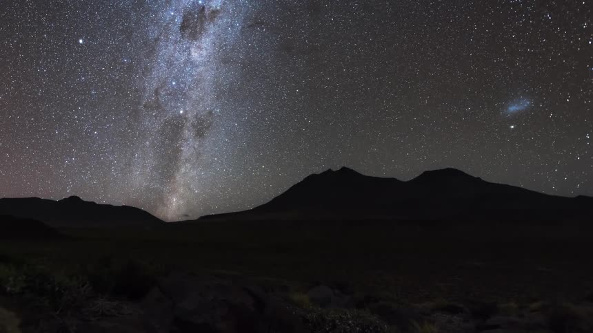 Time lapse of the stars on the night sky turning over the silhouette of mountains from dusk to dawn