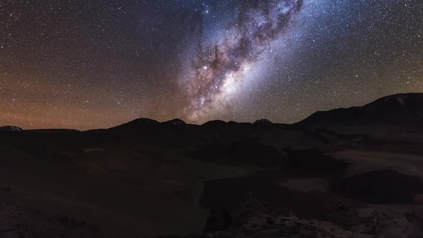 The milky way galaxy moves across the sky over a mountain range