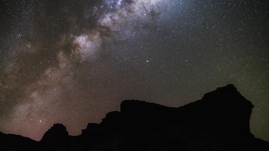 The milky way galaxy moves over a rock formation in the night sky