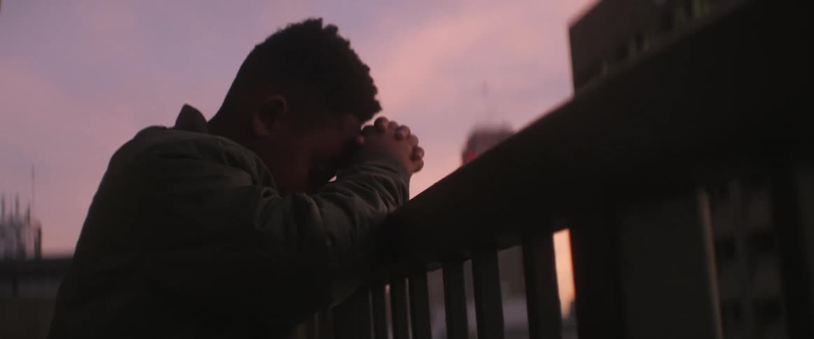 A man with his hands crossed and head down leaning on the porch of the house