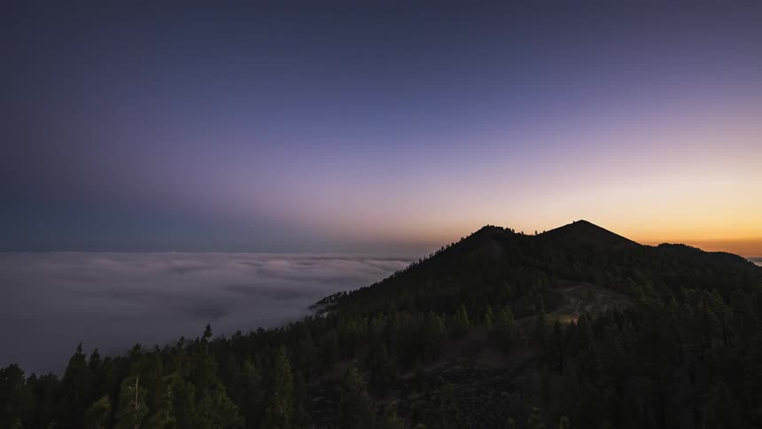 A mountain covered with a dense forest is seen beneath a beautiful sky
