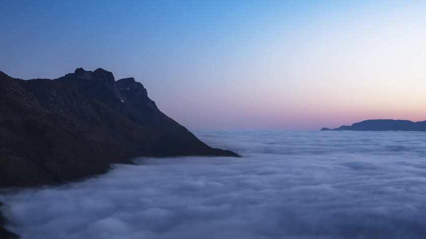 Time lapse of mountain tops protruding over a layer of moving clouds at morning