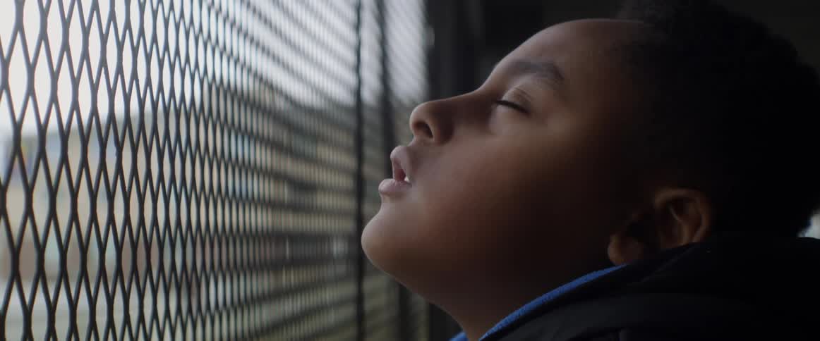 Close up of the face of a young girl looking out through a fence at daytime