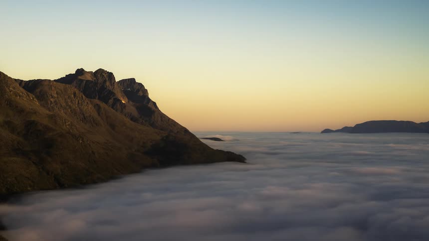 Mountain ridges poke through a sea of clouds as the sun rises