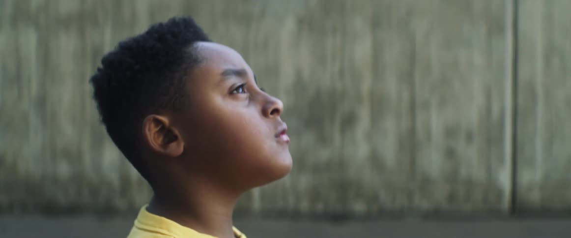 Boy wearing yellow t shirt walks in basketball court looking up in the sky