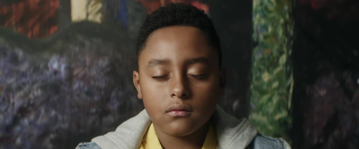 Youth stands with eyes closed in front of large artwork