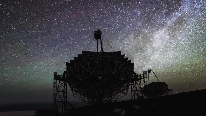 Countless stars fill the nighttime sky as two large telescopes point upwards at the sky