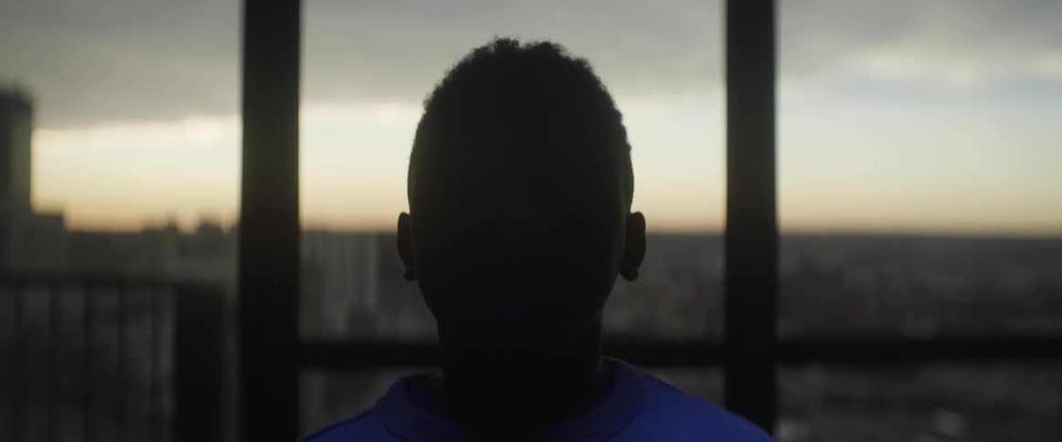 Youth stands near window staring as flashing lights color his face blue then red