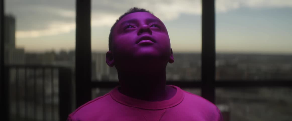 A young boy looks upwards as a purple light shines upon his face