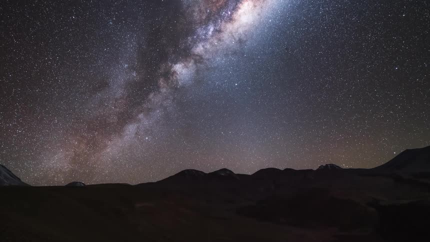 The stars in the night sky glow as the milky way rises over the mountains