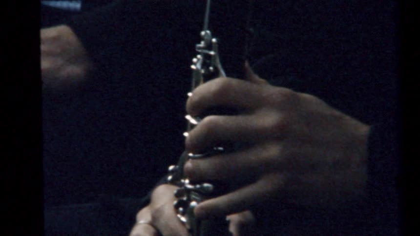A man is playing a clarinet next to a man sitting down