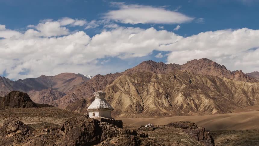 Clouds pass over a small building on an arid mountain ridge during the day