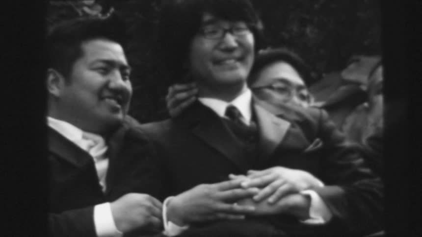 Men in suit an glasses put hands on top of each other and poses for the camera smiling