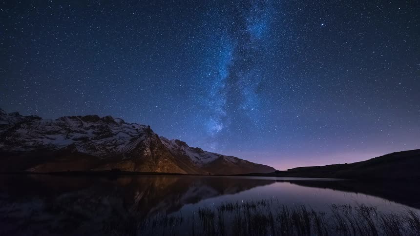Water reflects snow covered mountains and starry sky at night