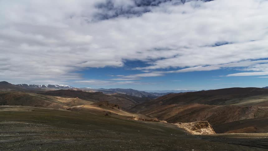 A time lapse shows clouds passing above a valley lined with hills and mountains