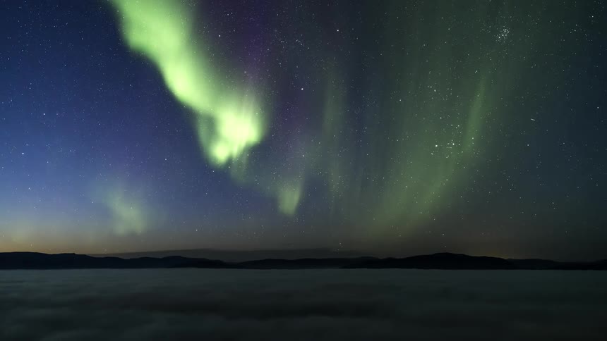 Green lights of the aurora borealis glow in the night sky among the stars as daylight arrives