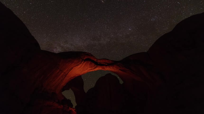 Night sky moves slowly over highlighted red stone arch