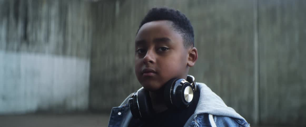 A boy is standing outside near a building with headphones around his neck